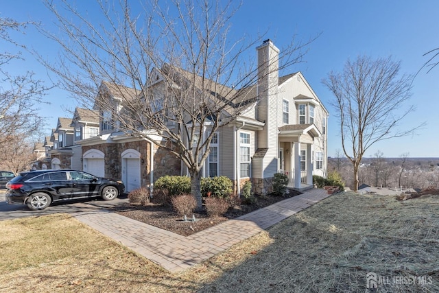 view of front of house featuring a front lawn, driveway, stone siding, a garage, and a chimney