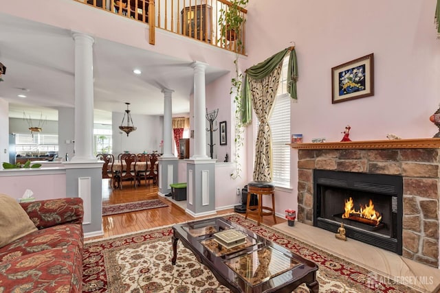 living area featuring a fireplace, baseboards, ornate columns, and wood finished floors