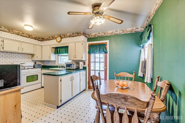 kitchen featuring a sink, a peninsula, dark countertops, ceiling fan, and white gas range oven