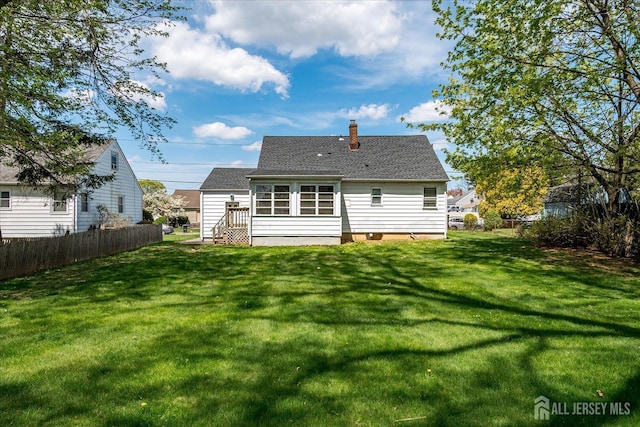 back of house with fence, a chimney, a yard, and roof with shingles