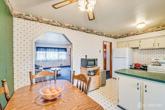 dining room featuring arched walkways, ceiling fan, wallpapered walls, and light floors
