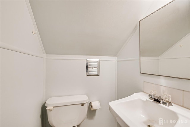 bathroom featuring visible vents, toilet, a sink, backsplash, and vaulted ceiling