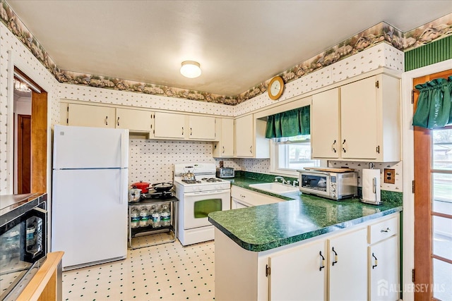 kitchen with white appliances, a peninsula, wallpapered walls, and dark countertops