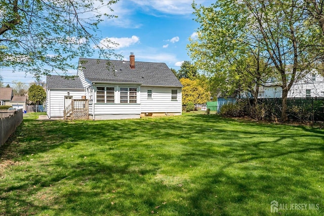 back of house featuring a yard, fence, a chimney, and a shingled roof