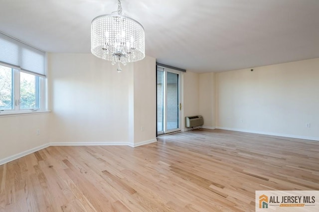 empty room with an AC wall unit, baseboards, an inviting chandelier, and wood finished floors