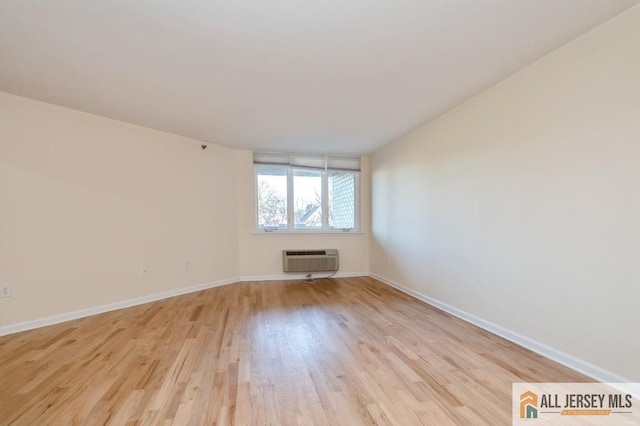 empty room with light wood-style floors, baseboards, and a wall unit AC