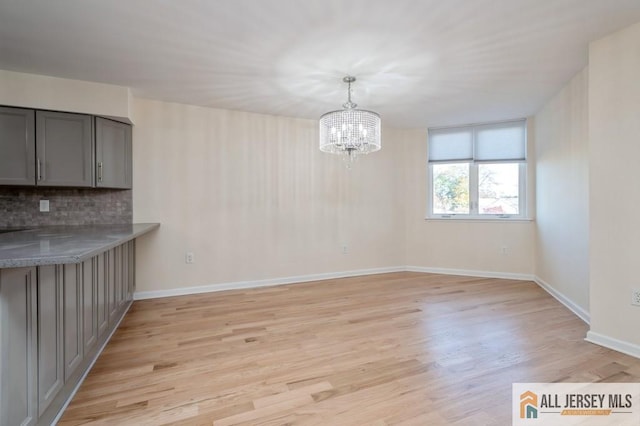 unfurnished dining area with an inviting chandelier, baseboards, and light wood finished floors