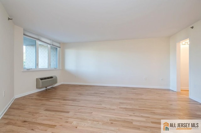 empty room with baseboards, light wood-style flooring, and a wall mounted air conditioner