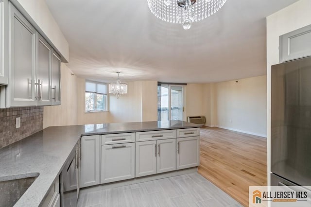 kitchen with a peninsula, light stone countertops, baseboards, a chandelier, and backsplash