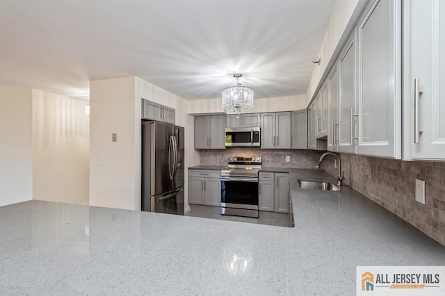 kitchen with a sink, a chandelier, gray cabinets, stainless steel appliances, and tasteful backsplash