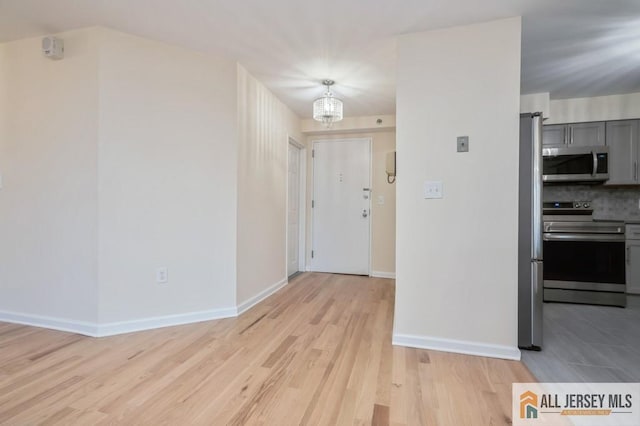 interior space with a notable chandelier, gray cabinets, stainless steel appliances, baseboards, and light wood-type flooring