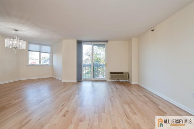 unfurnished room featuring baseboards, a wall mounted AC, light wood-type flooring, and a chandelier