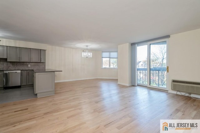 unfurnished living room featuring an AC wall unit, baseboards, an inviting chandelier, and light wood-style floors