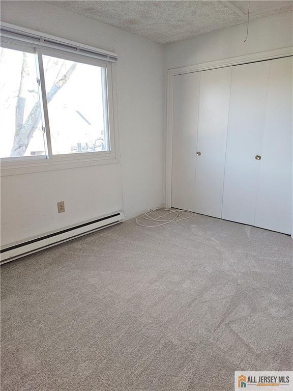 unfurnished bedroom featuring a textured ceiling, a baseboard heating unit, a closet, and light carpet