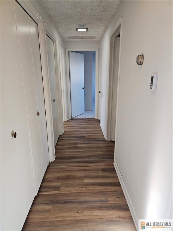 corridor with a textured ceiling and dark hardwood / wood-style floors