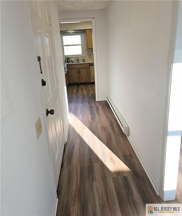 hall with a textured ceiling, a baseboard heating unit, dark wood-style flooring, a sink, and baseboards