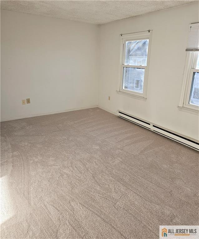 empty room featuring a textured ceiling, light carpet, and a baseboard radiator