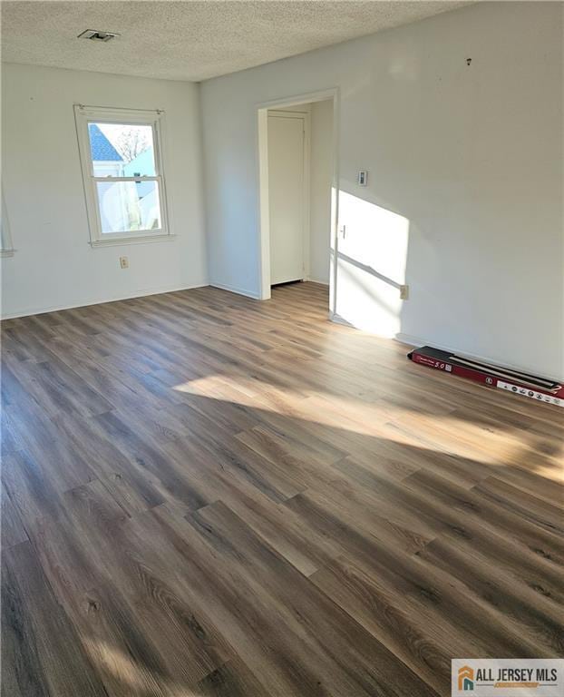 unfurnished room with visible vents, dark wood-style flooring, and a textured ceiling