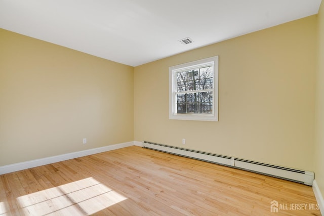empty room featuring wood finished floors, baseboards, baseboard heating, and visible vents