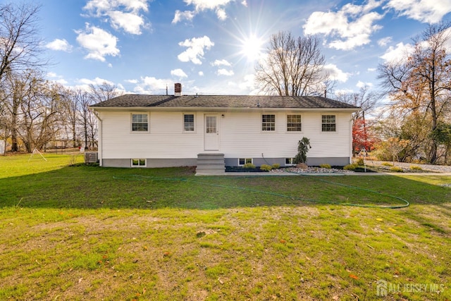 rear view of property with a chimney, entry steps, and a lawn