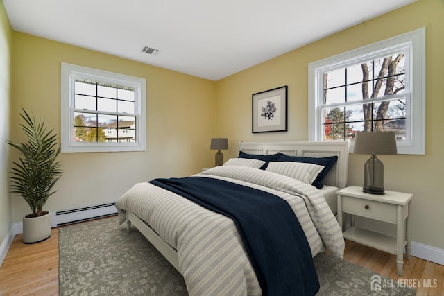 bedroom with a baseboard heating unit, wood finished floors, visible vents, and baseboards