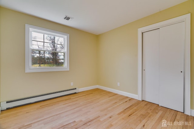 unfurnished bedroom featuring wood finished floors, a closet, baseboard heating, baseboards, and visible vents