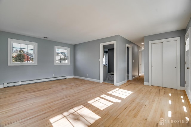 interior space with a baseboard heating unit, baseboards, visible vents, and light wood finished floors