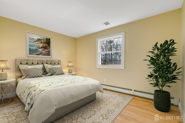 bedroom with a baseboard radiator, wood finished floors, and visible vents