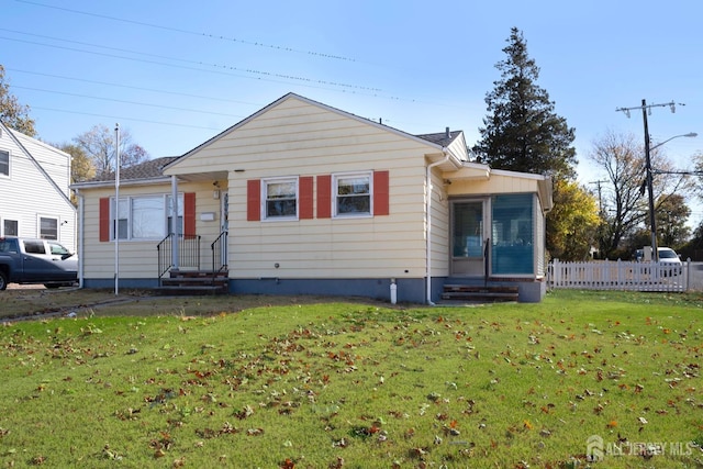 bungalow-style home with entry steps, a front lawn, and fence