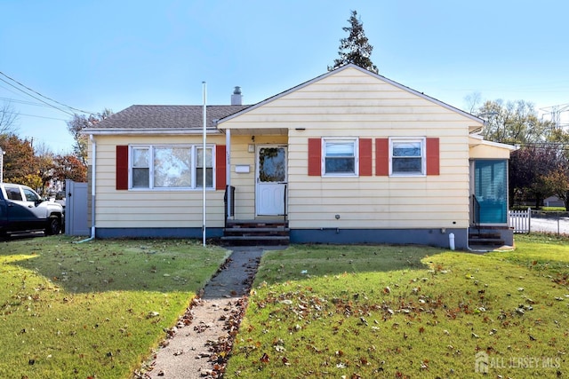 view of front facade featuring entry steps, a shingled roof, a front lawn, and fence