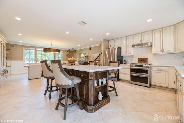 35 Winthrop Dr, Manalapan, NJ 07726 - kitchen featuring appliances with stainless steel finishes, under cabinet range hood, cream cabinets, a kitchen bar, and crown molding