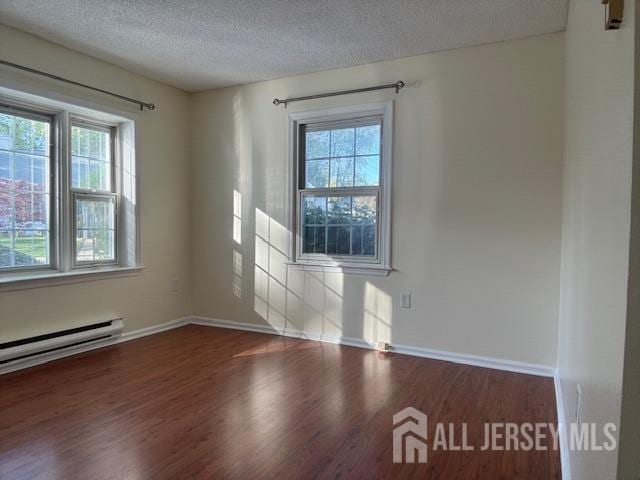 empty room featuring a healthy amount of sunlight, a textured ceiling, baseboards, and wood finished floors
