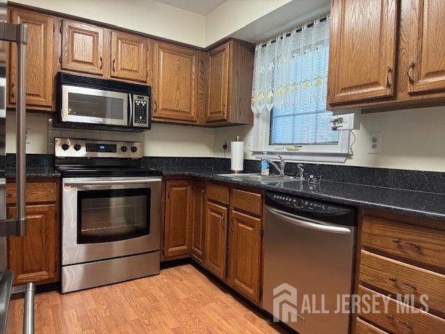 kitchen with a sink, brown cabinets, dark countertops, and stainless steel appliances