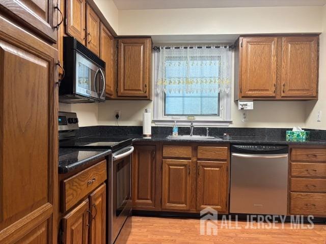 kitchen featuring light wood-style floors, a sink, brown cabinetry, and stainless steel appliances