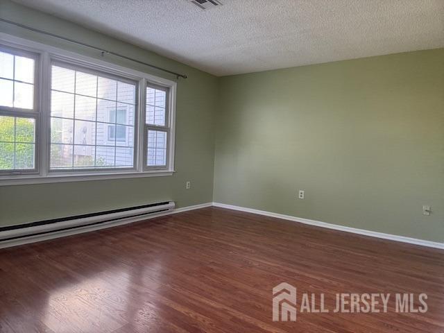 empty room with visible vents, wood finished floors, baseboards, baseboard heating, and a textured ceiling