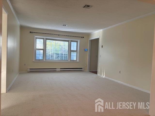 empty room featuring crown molding, carpet floors, baseboard heating, and visible vents