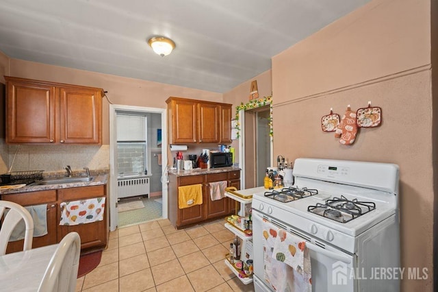 kitchen featuring light tile patterned floors, radiator, gas range gas stove, and sink