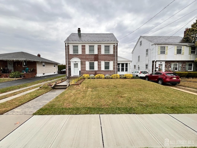 view of front of property featuring a chimney, a front lawn, and brick siding