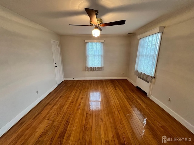 empty room with ceiling fan, radiator, hardwood / wood-style floors, and a wealth of natural light