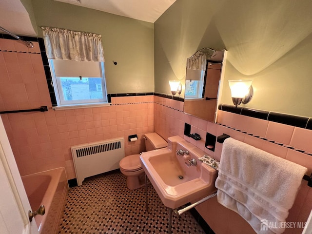 bathroom with sink, radiator, tile walls, and toilet