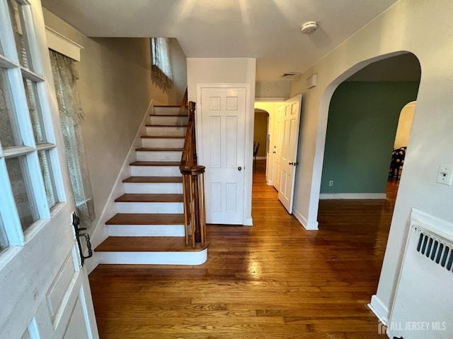 stairway with arched walkways, visible vents, baseboards, and wood finished floors