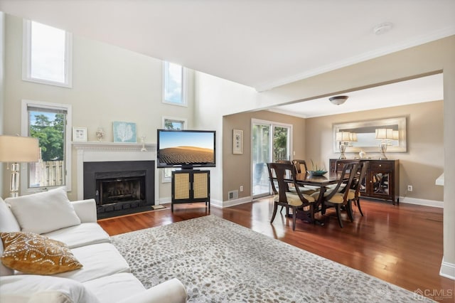 living area featuring baseboards, wood finished floors, a fireplace with flush hearth, and crown molding