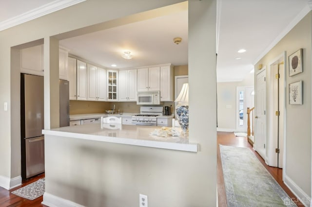 kitchen featuring white appliances, a peninsula, white cabinetry, glass insert cabinets, and light countertops