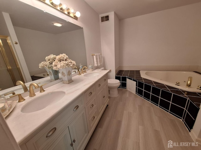 bathroom featuring wood finished floors, a tub with jets, double vanity, and a shower with shower door