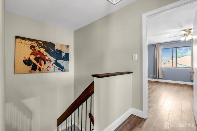 corridor with baseboards, an upstairs landing, and wood finished floors