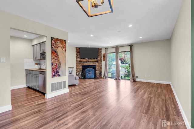 unfurnished living room with visible vents, a large fireplace, wood finished floors, baseboards, and a notable chandelier