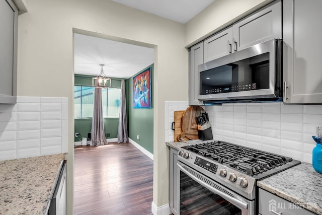 kitchen featuring backsplash, appliances with stainless steel finishes, light stone countertops, wood finished floors, and baseboards