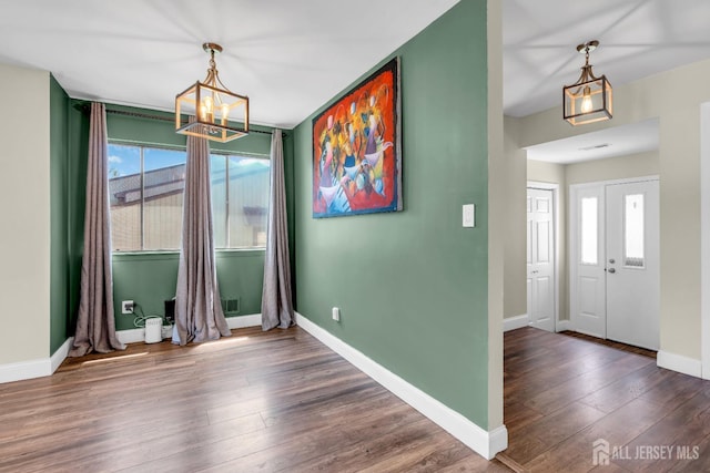 unfurnished dining area with baseboards, a notable chandelier, and hardwood / wood-style flooring