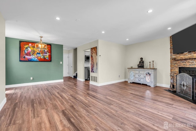 unfurnished living room featuring a stone fireplace, wood finished floors, stairway, baseboards, and recessed lighting