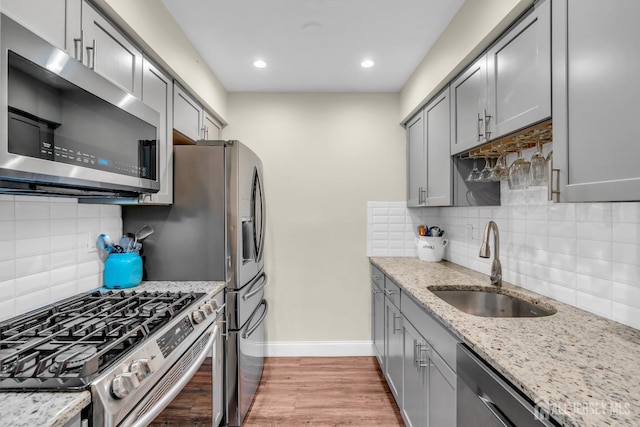 kitchen featuring baseboards, a sink, light wood finished floors, gray cabinetry, and stainless steel appliances